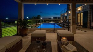 An outdoor pool area with lounge chairs and a table, surrounded by a pergola and a stone wall.