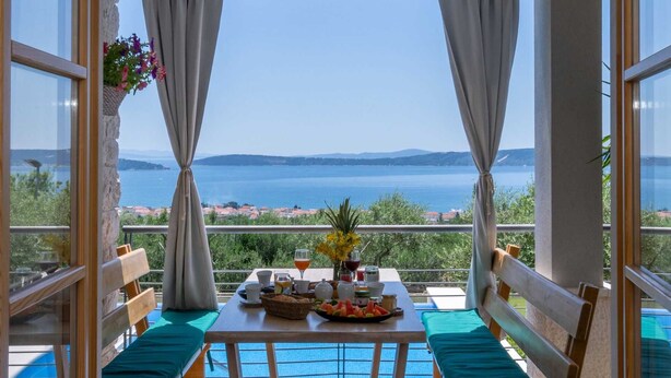 A balcony with a table set for breakfast, overlooking a body of water and a distant coastline.