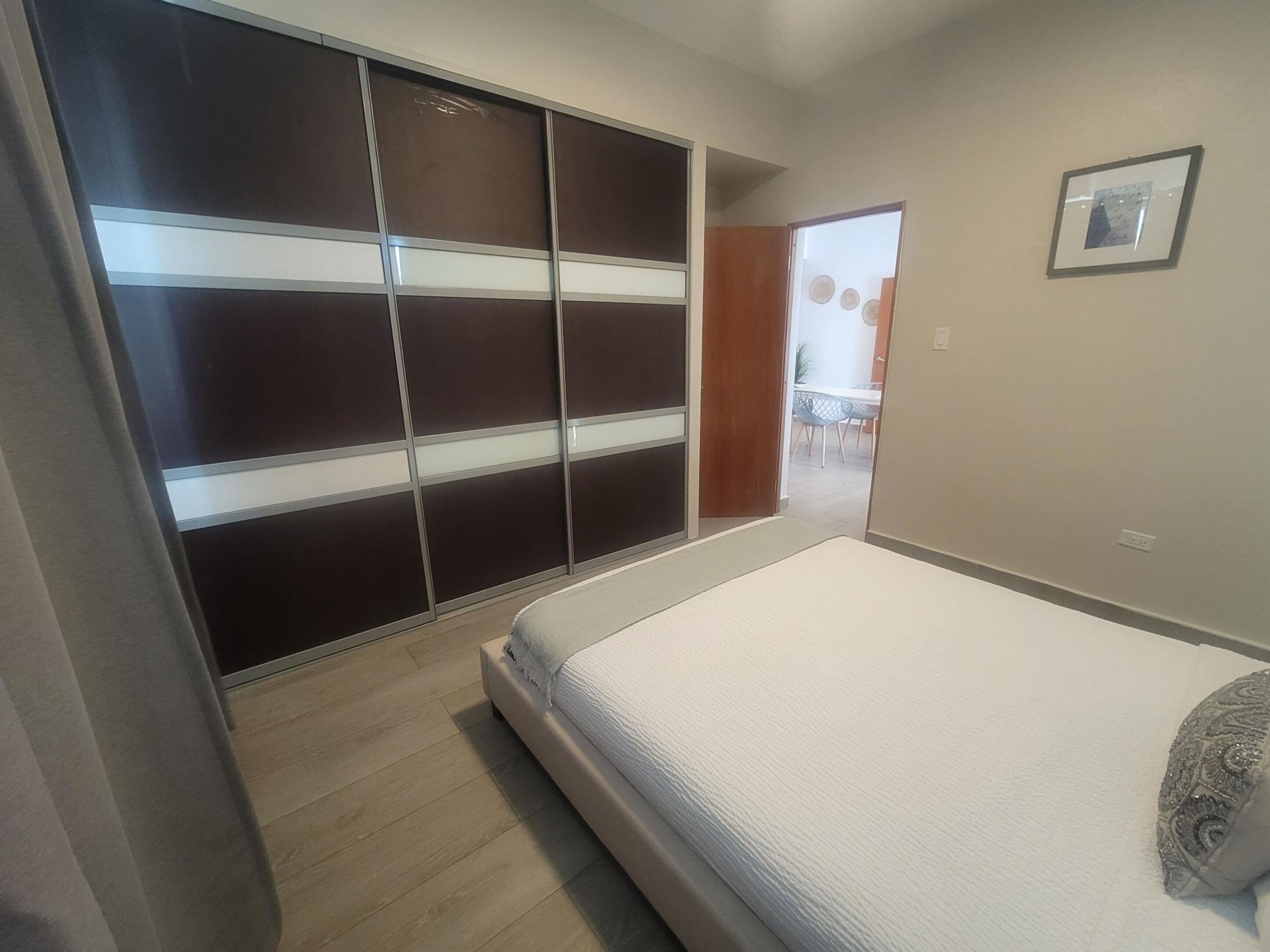 Un dormitorio con cama, armario y puerta que da a un comedor.