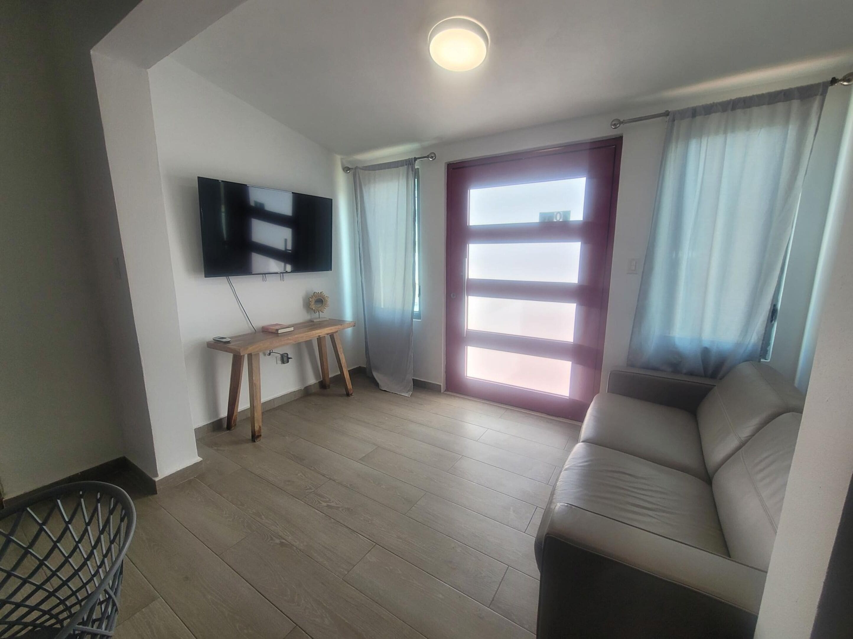 A living room with a sofa, a TV mounted on the wall, a wooden table, and a door with a frosted glass panel.
