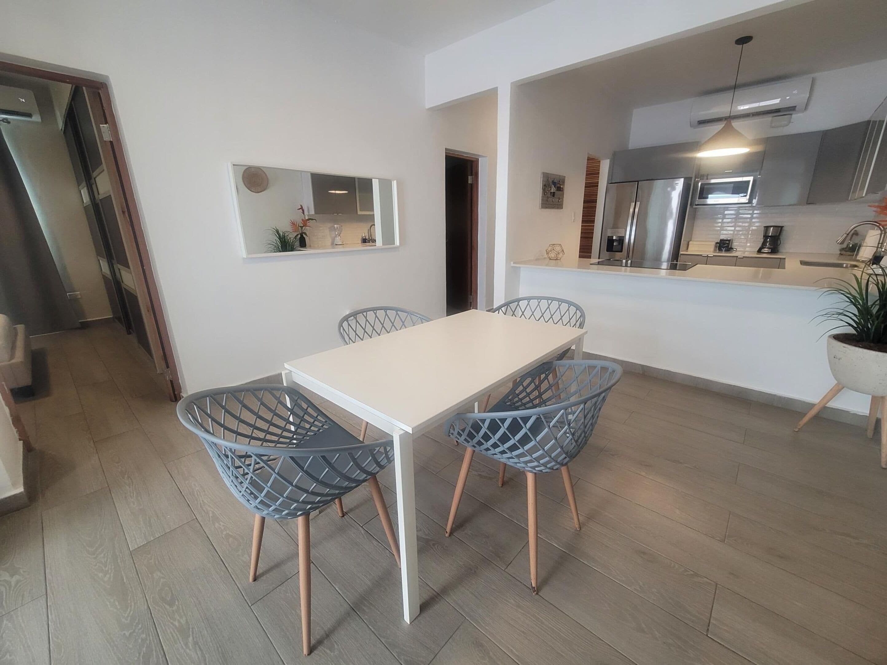 A modern kitchen with a microwave, stove, and sink. There is a dining area with a white table and four chairs.