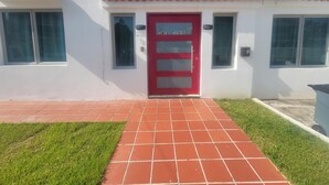 A white building with a red door, numbered 2058, and a tiled walkway leading to it.
