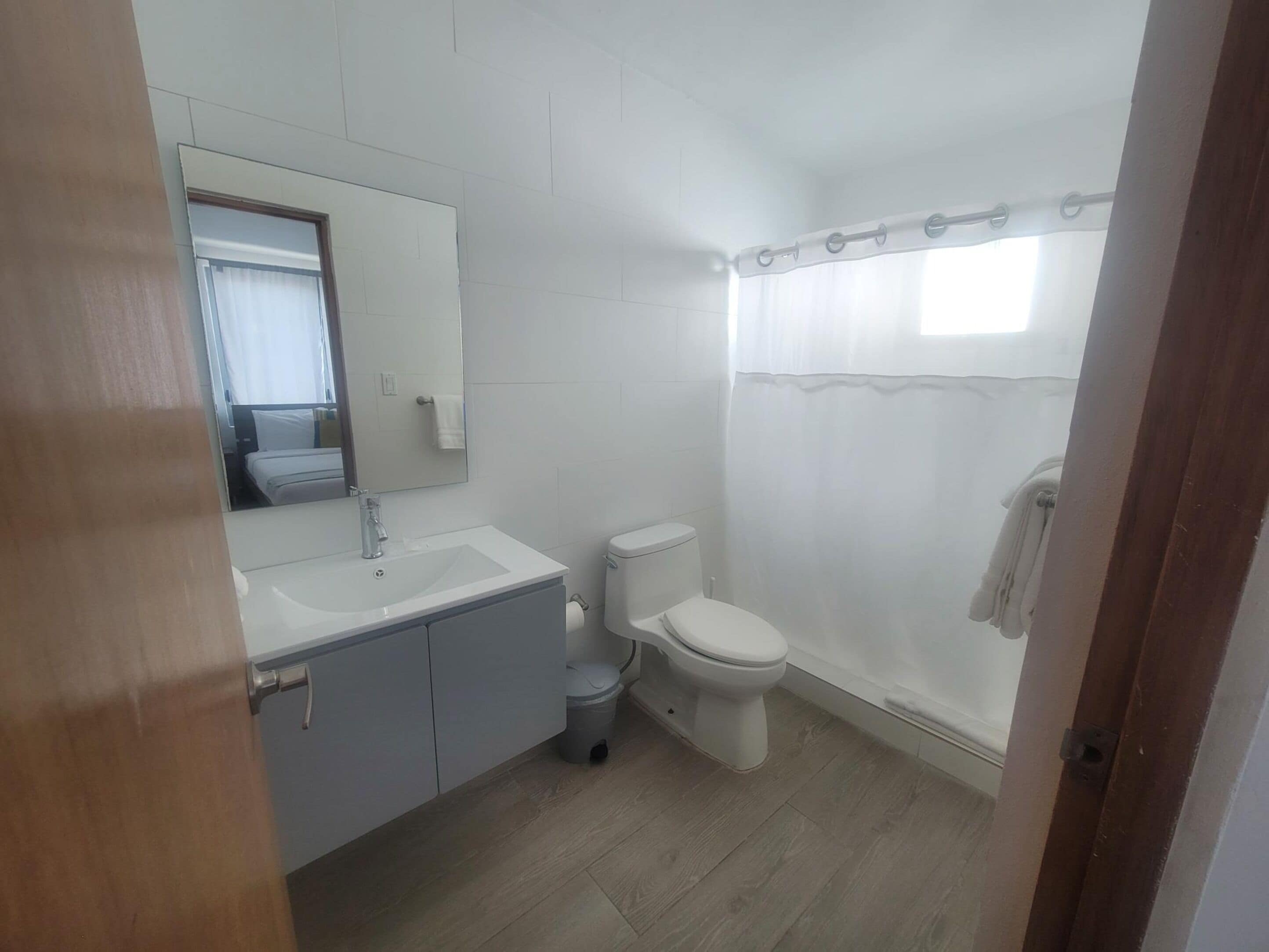 Un bagno con lavandino bianco, specchio, water e tenda per la doccia.