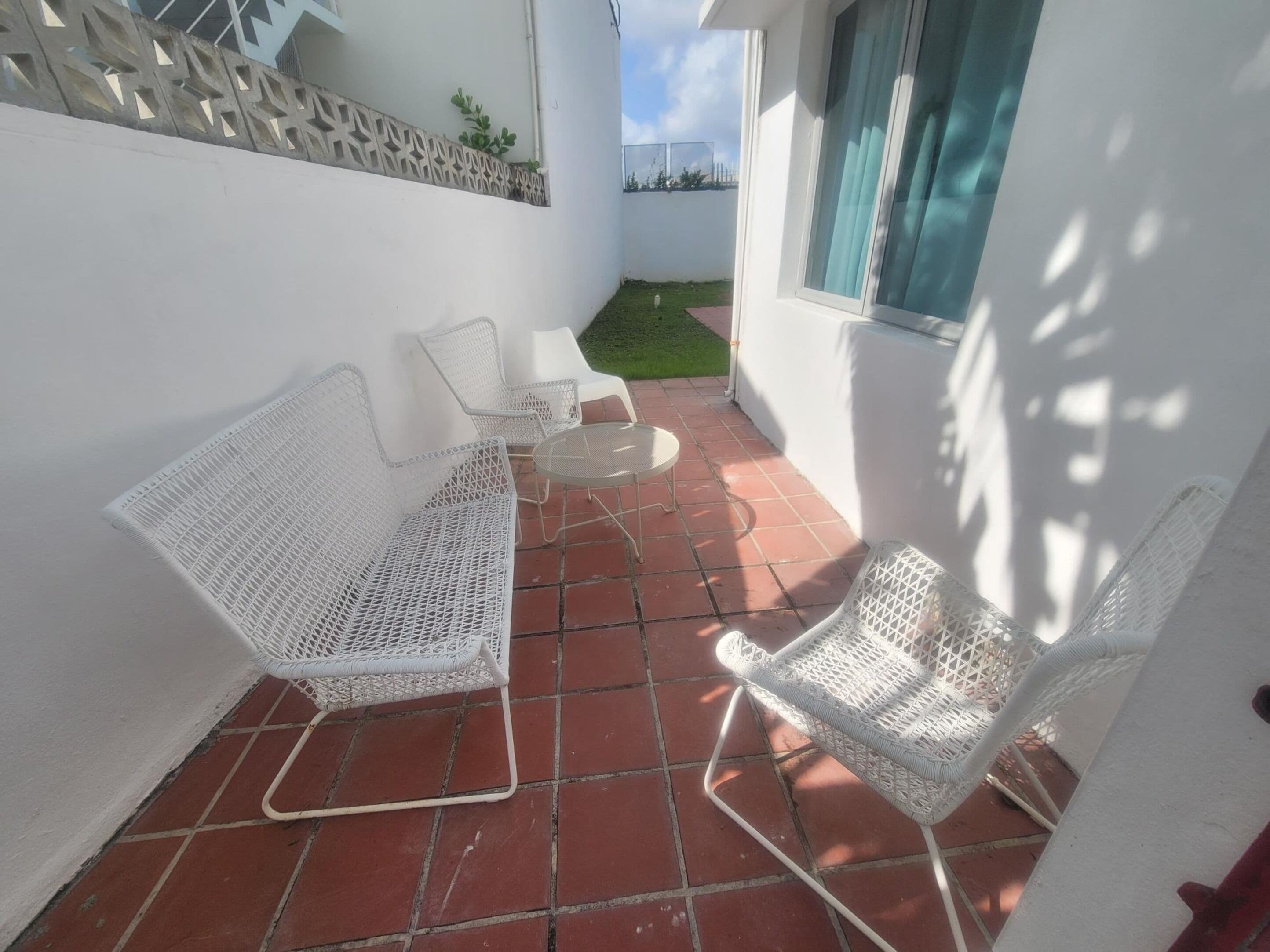 Une terrasse dotée de meubles en osier blanc, comprenant deux chaises et une petite table, posée sur un sol carrelé de tuiles rouges.