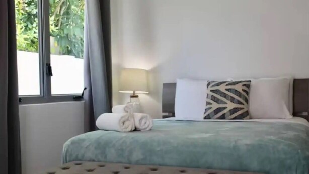 A hotel room with a bed, a nightstand, a lamp, and a window with curtains.