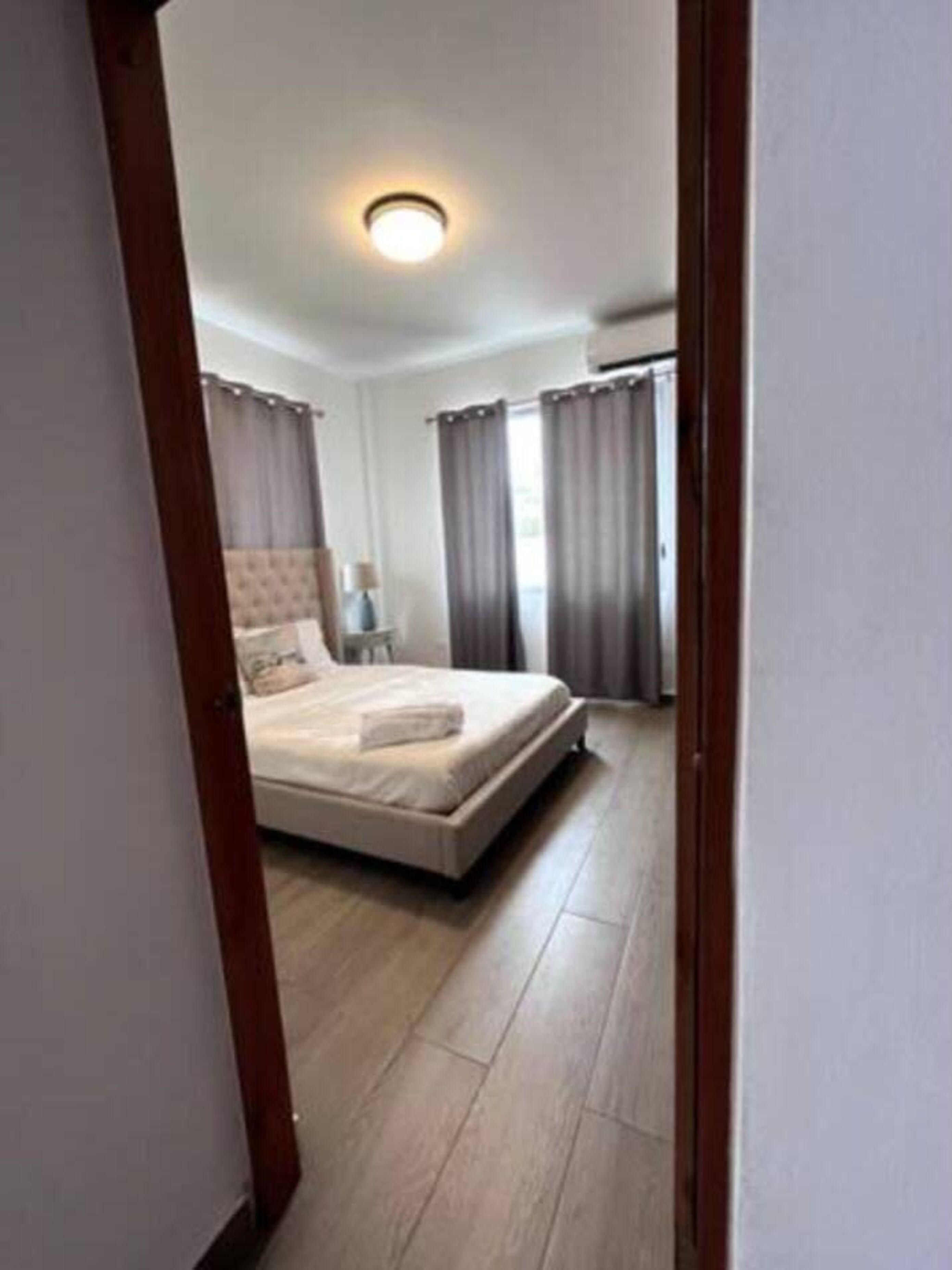 Un dormitorio con cama, mesita de noche, lámpara y ventana con cortinas.
