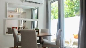 A modern dining area with a round table and four chairs, large windows with curtains, and a ceiling-mounted air conditioning unit.
