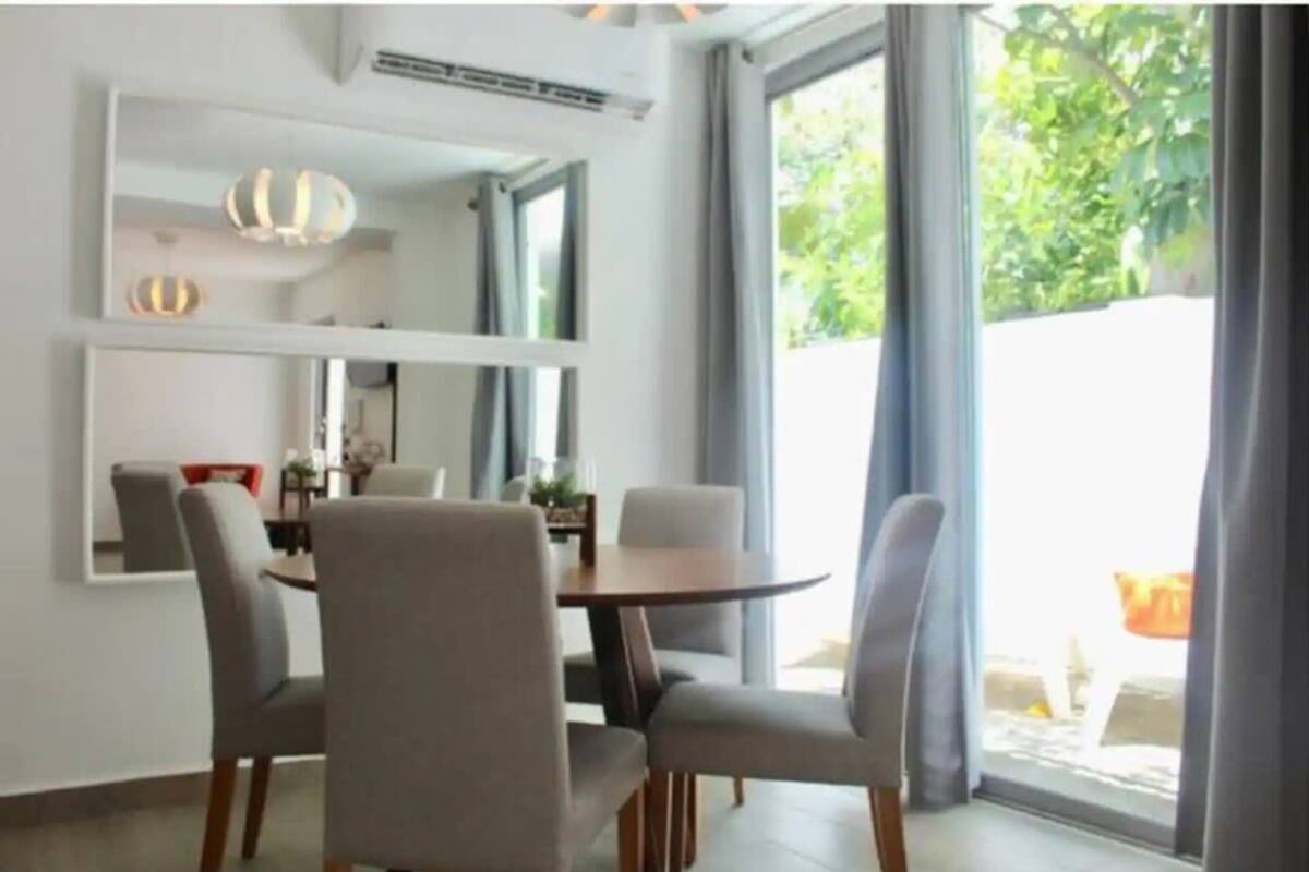 Un comedor moderno con una mesa redonda y cuatro sillas, ventanas amplias con cortinas y un equipo de aire acondicionado instalado en el techo.