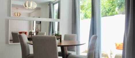 A modern dining area with a round table and four chairs, large windows with curtains, and a ceiling-mounted air conditioning unit.