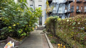 A narrow alleyway with a wooden bench, a concrete path, and a chain-link fence.