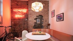 A dining area with a neon sign indicating meal times, a bicycle, and a brick wall.