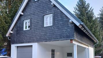 Ein zweistöckiges Haus mit dunklem Schindeldach, weißen Außenwänden und einer Veranda mit zwei Stühlen.
