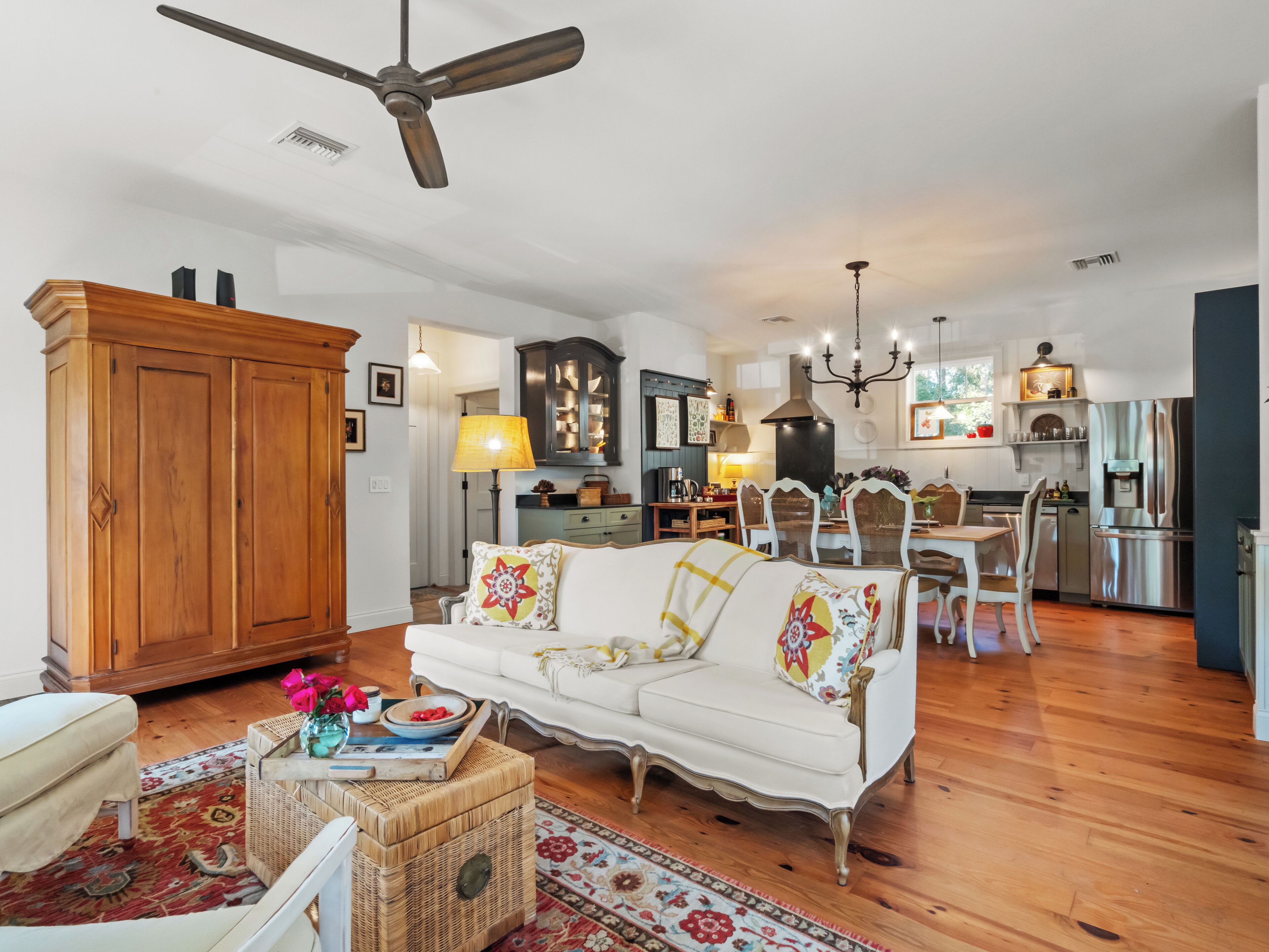 A spacious living room with a white sofa, wooden cabinet, and a dining area with a chandelier.