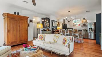 A spacious living room with a white sofa, wooden cabinet, and a dining area with a chandelier.