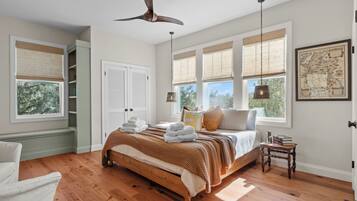 A spacious bedroom with a large bed, wooden flooring, and multiple windows.