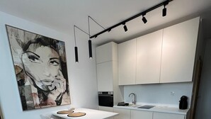 A modern kitchen with white cabinetry, a central island with bar stools, a black oven, and a coffee machine.
