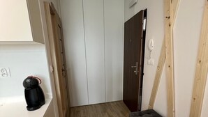 A narrow hallway with a white wardrobe, a black sofa, and a coffee maker on a counter.
