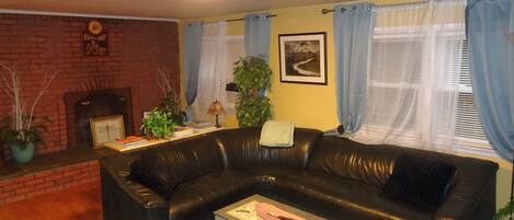 A living room with a black leather sofa, a small table with a pink basket, a fireplace, and a framed picture on the wall.