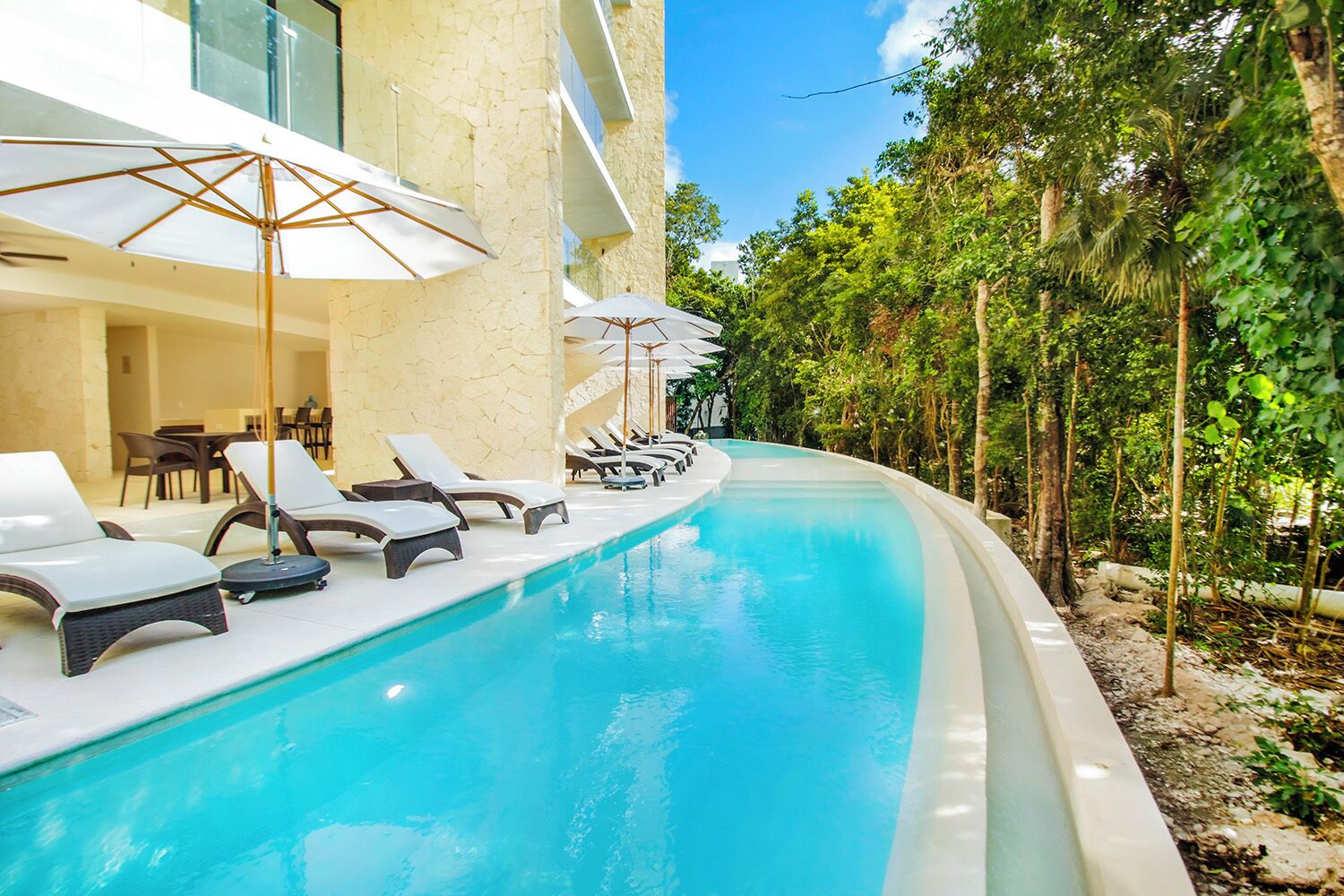 A poolside area with lounge chairs and umbrellas, surrounded by greenery.