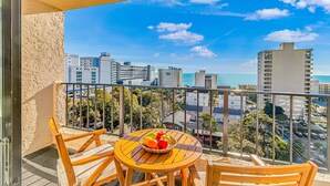 Een balkon met een tafel en stoelen, een mand vol fruit en een uitzicht over de stad.
