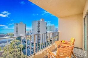 A balcony with a table and chairs, overlooking a cityscape with tall buildings and a clear blue sky.