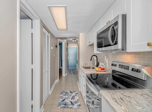 A modern kitchen with white cabinets, a stainless steel microwave, an oven, and a sink.