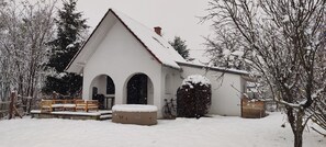 Un edificio cubierto de nieve con techo triangular, un porche con bancos y una bicicleta estacionada afuera.