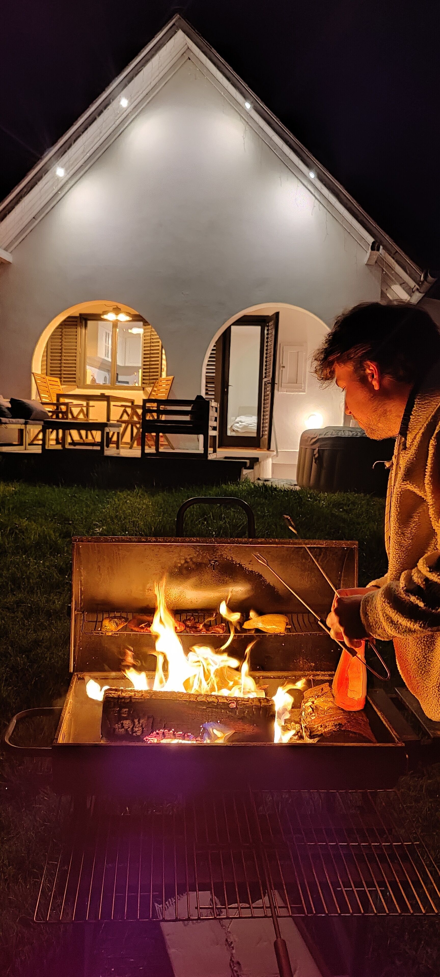 Eine Person grillt nachts im Freien, im Hintergrund ist ein Haus zu sehen.