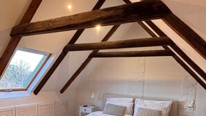 Ein Schlafzimmer mit geneigter Decke, Holzbalken, einem großen Bett, Nachttischen und einem Fenster.