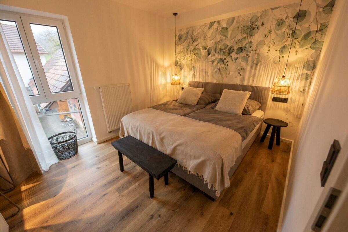 Un dormitorio con una cama grande, dos mesitas de noche, un banco, una ventana y un radiador.