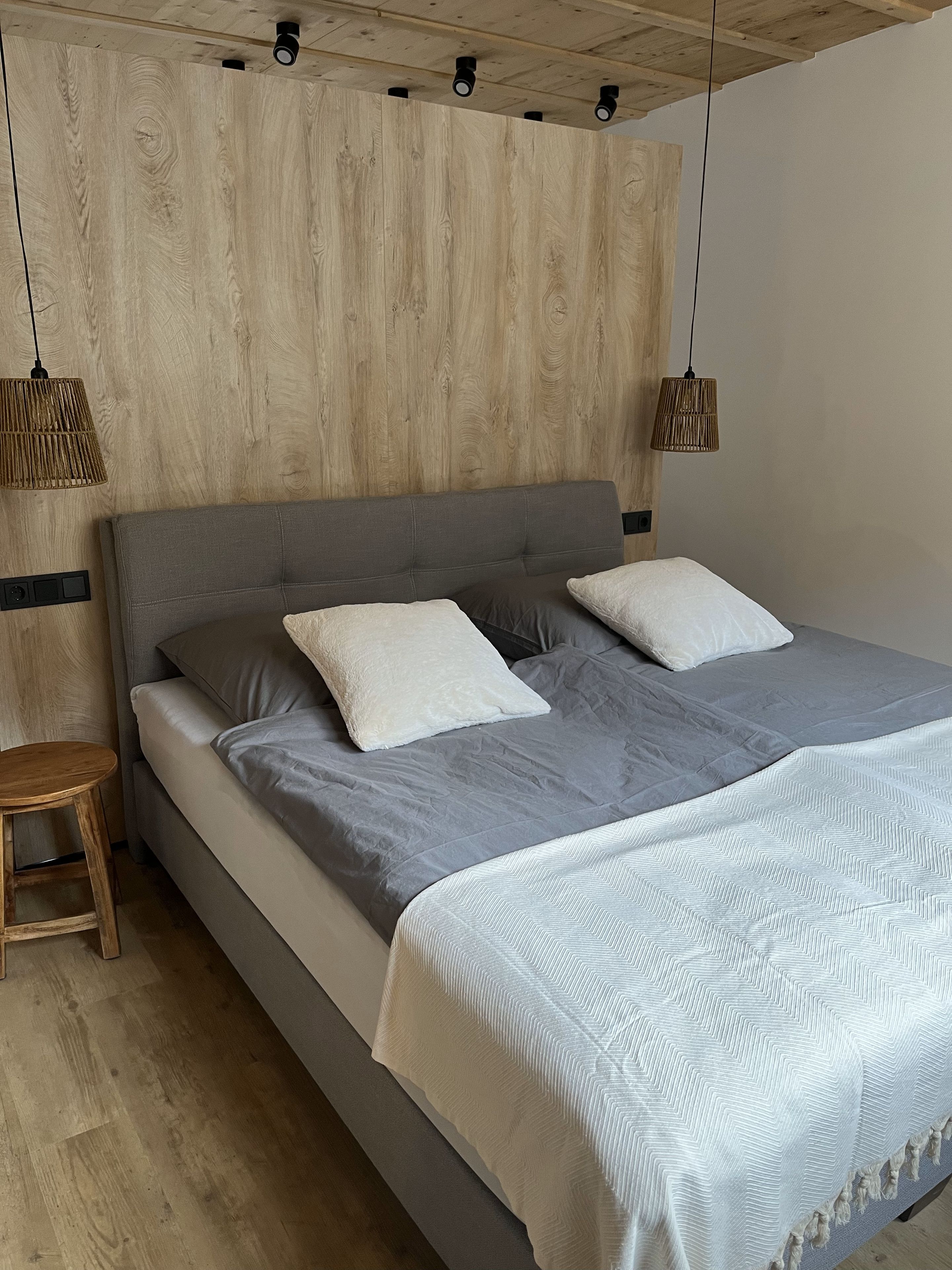 Ein Schlafzimmer mit einem hölzernen Kopfteil, zwei Nachttischlampen, einem grauen Sofa und einer geblümten Bettdecke.