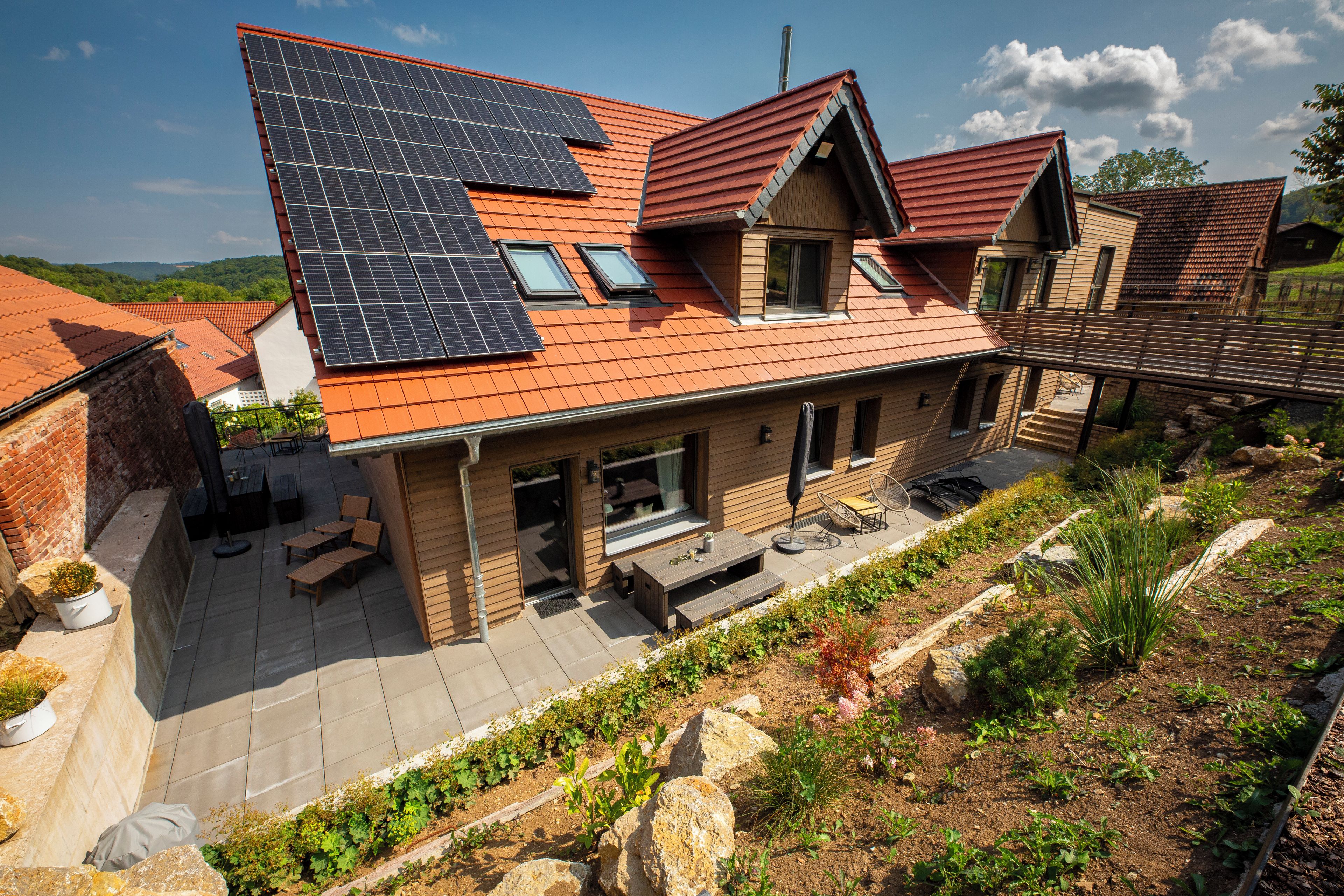 Ein modernes Haus mit Satteldach, Solaranlage und einer Terrasse mit Gartenmöbeln.