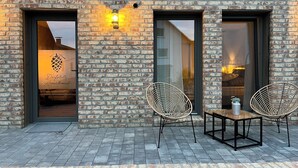 A brick building with two open doors and a window, a sign reading "Dorfplate Apartment," and two wicker chairs on a tiled patio. - Wyzenborne (Sontra)