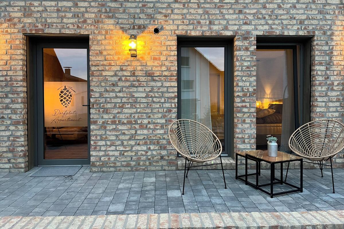 Un edificio de ladrillo con dos puertas abiertas y una ventana, un cartel que dice 