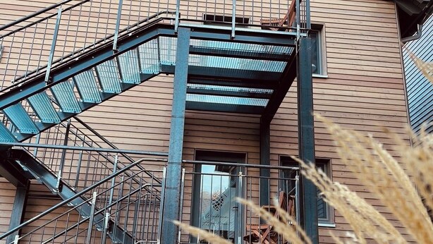 A multi-story building with a wooden facade, a metal staircase, and a brick base. - Wyzenborne (Sontra)