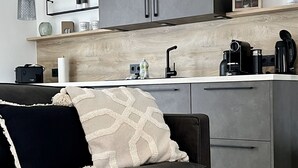 A modern kitchen with grey cabinets, a wooden countertop, and a black sofa with a patterned throw pillow. - Wyzenborne (Sontra)