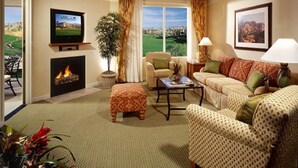 Un salon doté d’une cheminée, d’un téléviseur, d’un canapé et offrant une vue sur un terrain de golf.