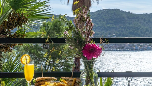 Une table avec un sandwich, des frites, un verre de jus d’orange et un vase rempli de fleurs.
