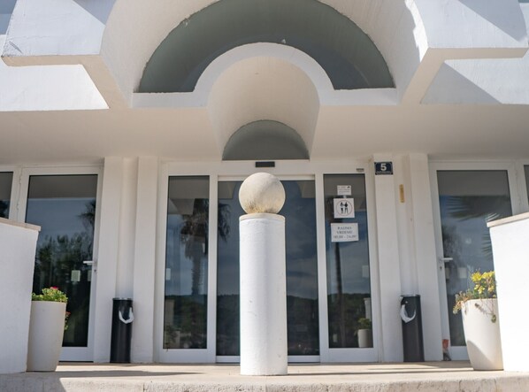 A building entrance with a white facade, a large spherical sculpture in the center, and a sign indicating a parking area. - Hotel Issa - Double Room Sea View 4 (Vis)