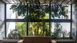 A room with a large window, a beige sofa, and a view of greenery outside.