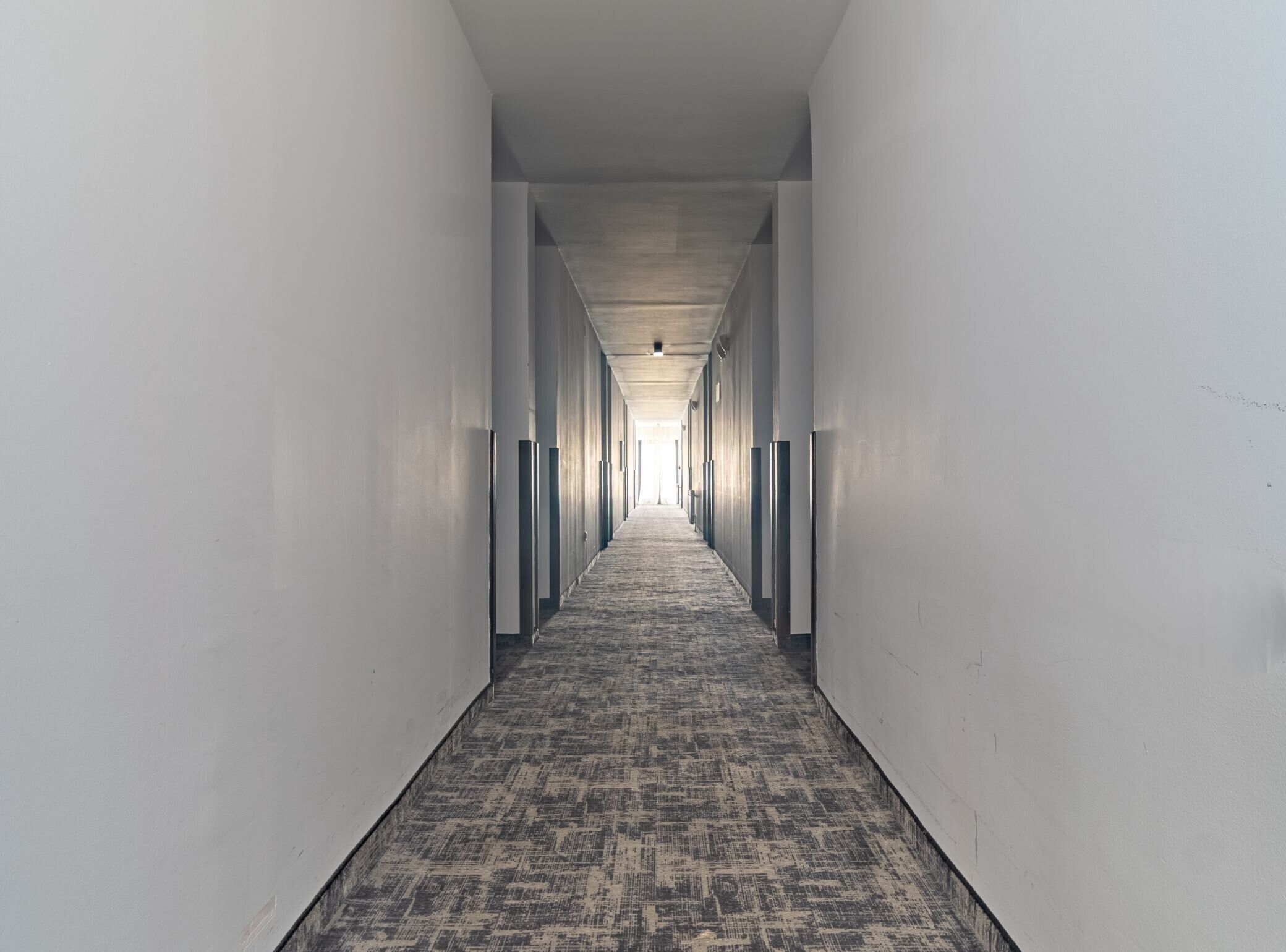 Un long couloir étroit, doté d’un tapis à motifs et de murs blancs.