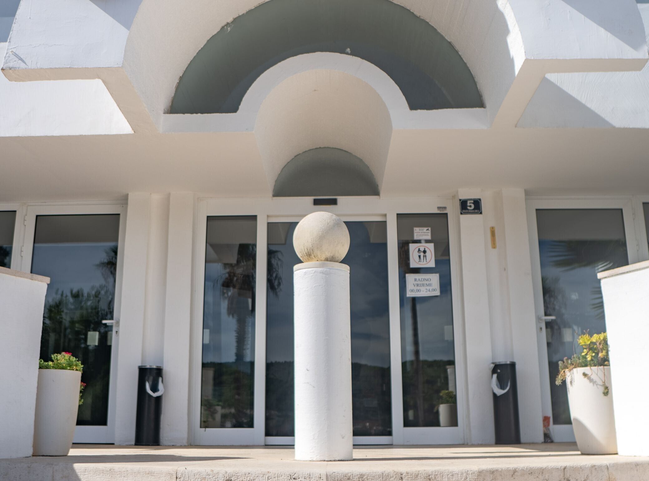 A building entrance with a white facade, a large spherical sculpture in the center, and a sign indicating a parking area.