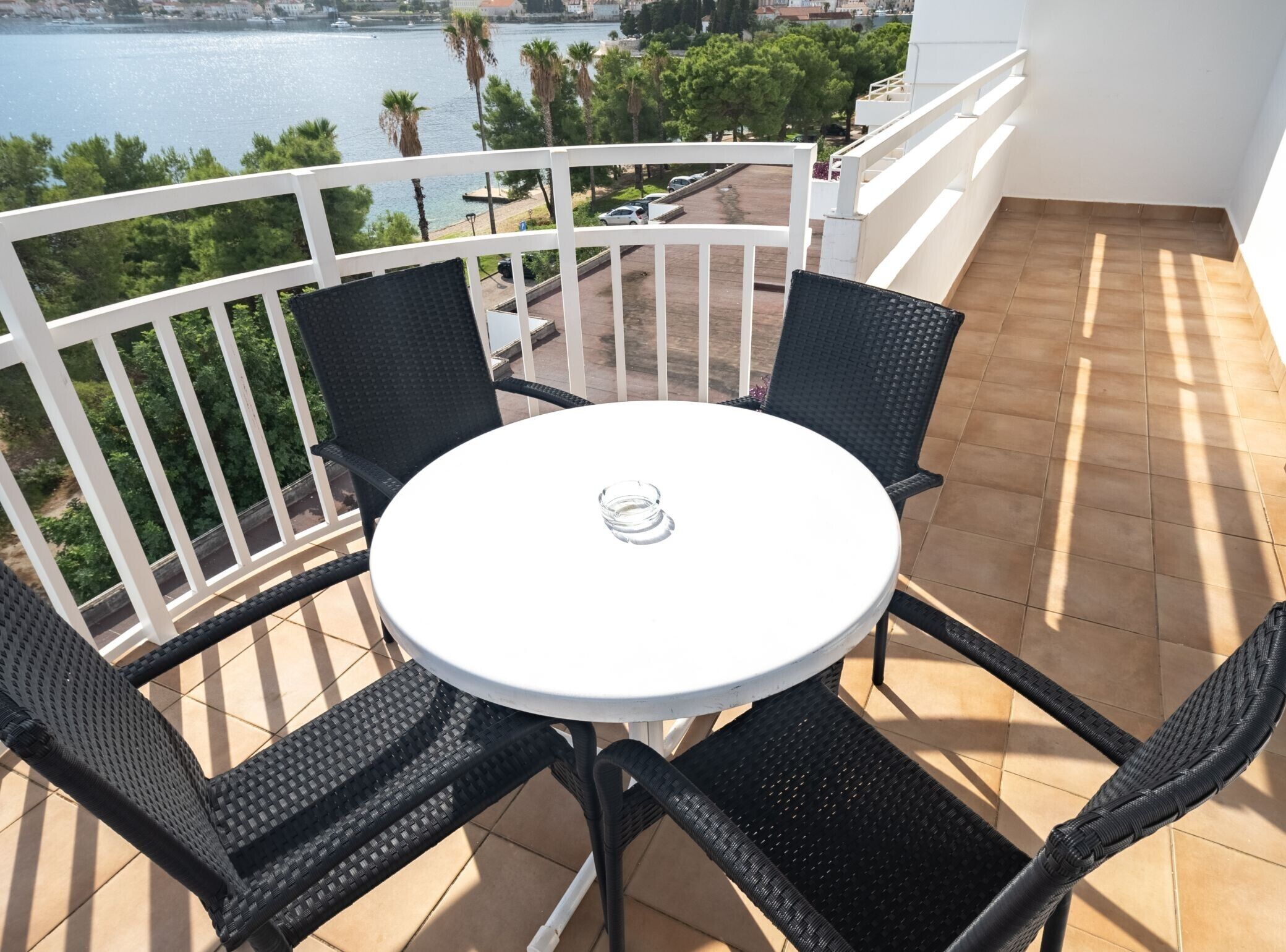 A balcony with a round table and four chairs, overlooking a body of water and a cityscape.