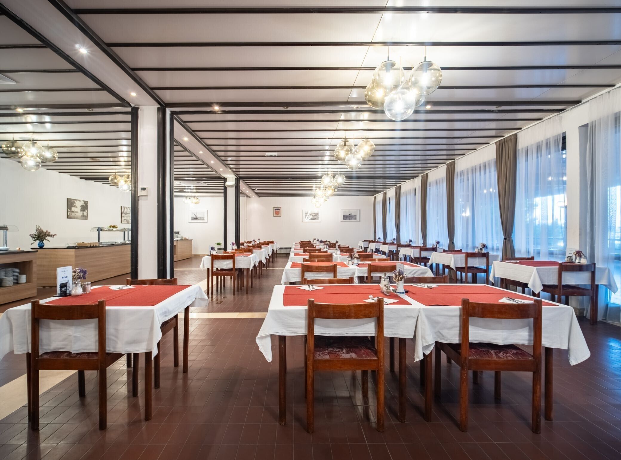 A spacious dining area with multiple tables and chairs, a reception desk, and large windows allowing natural light.