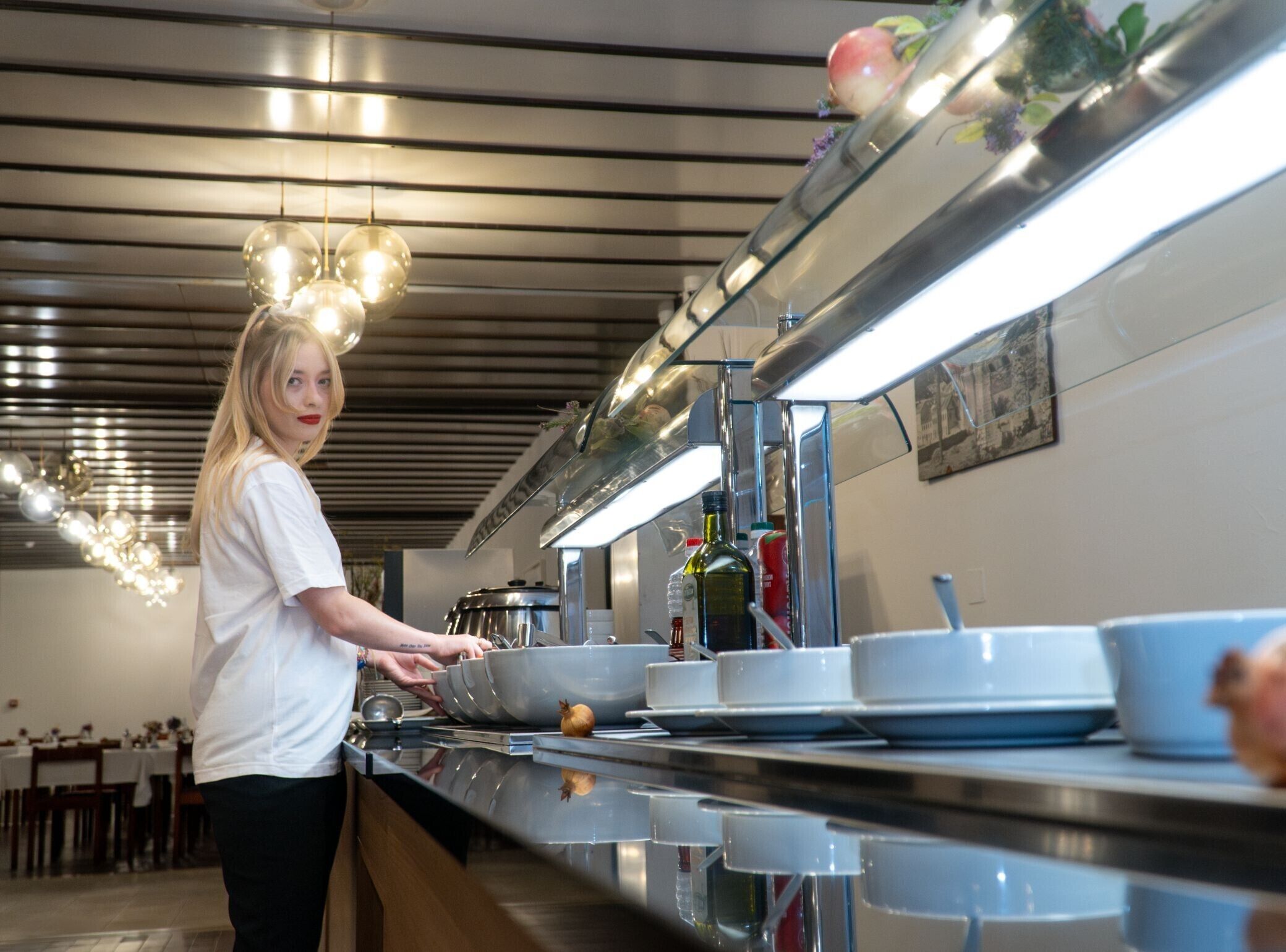 Een keuken met roestvrijstalen apparatuur, hangende lampen en iemand die kookt.