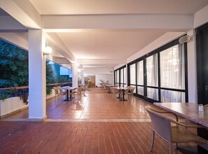 A spacious indoor area with multiple tables and chairs, large windows, and a brick floor. - Hotel Issa - Double Room Sea View 13 (Vis)