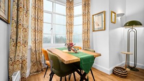 Ein Essbereich mit einem Holztisch, grünen Stühlen, gemusterten Vorhängen und einem Fenster mit Blick.