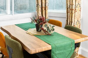 Una mesa de comedor con mantel verde, dos plantas en macetas y un camino de mesa tejido.