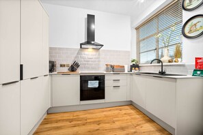 A modern kitchen with white cabinets, a black oven, and a window with blinds. - Stylish Two Bedroom Apartment - 2 Parking Spaces - Balcony (Birmingham)