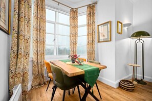 A dining area with a wooden table, green chairs, patterned curtains, and a window with a view. - Stylish Two Bedroom Apartment - 2 Parking Spaces - Balcony (Birmingham)
